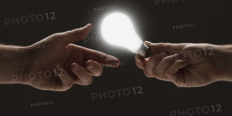 Hand passing a light bulb to another hand. Photo : Mike Kemp