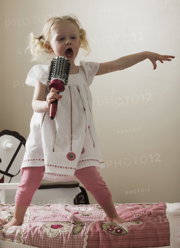 Young girl singing on her bed. Photo : Mike Kemp