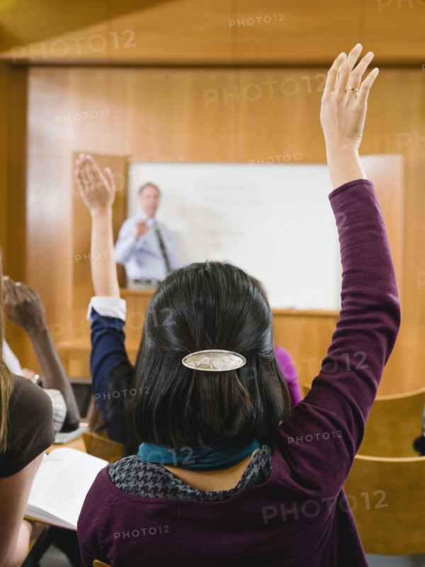 College students raising their hands in lecture hall.