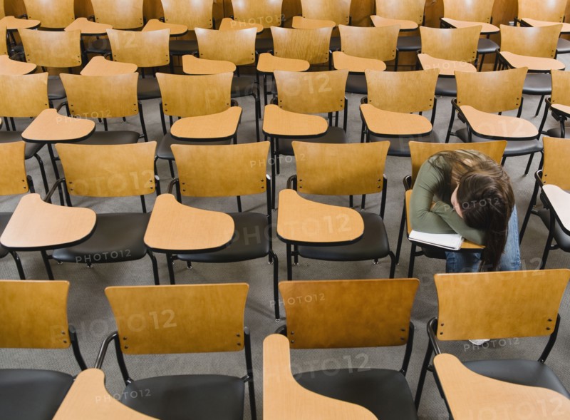 College student sleeping in empty lecture hall.