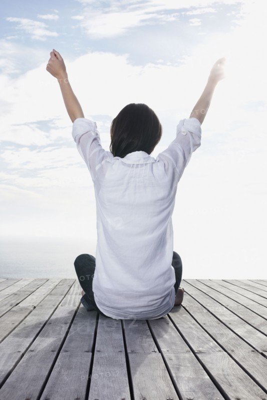 Woman sitting on porch with her arms raised. Photo : momentimages