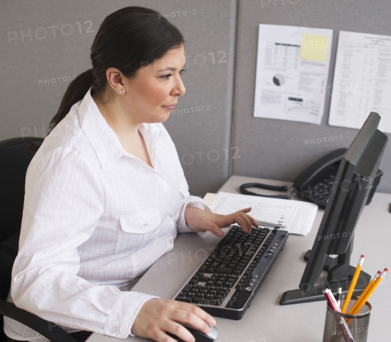 Businesswoman working on laptop in cubicle.