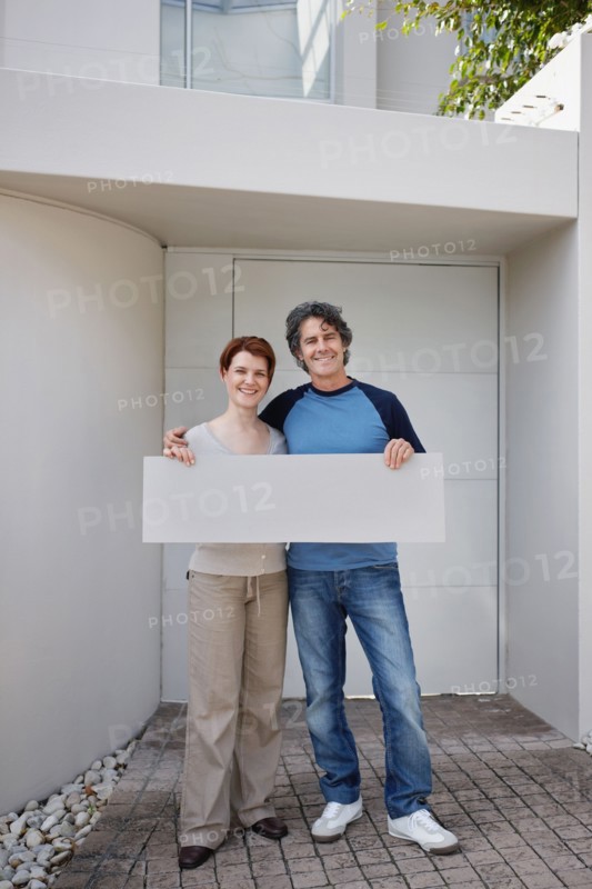 Couple standing in front of their home. Photo : momentimages
