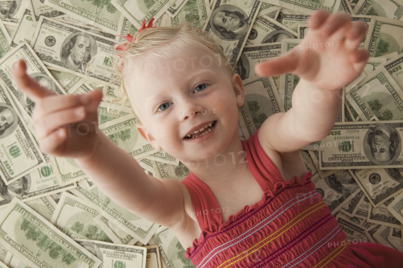 Young girl lying on a pile of money. Photo. Mike Kemp