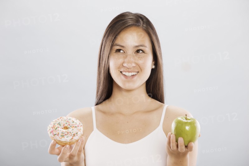 Woman holding an doughnut and an apple. Photo. FBP