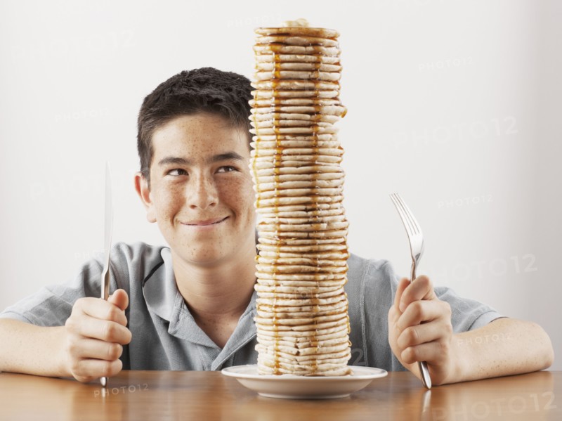 Young boy sitting behind a tall stack of pancakes. Photo. FBP