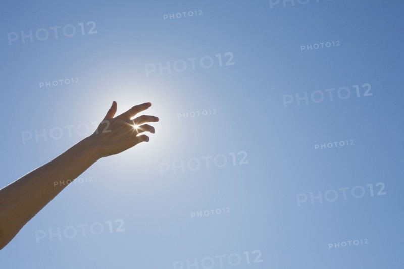 Hand in front of a sun flare in the sky. Photo : Chris Hackett