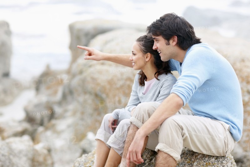 Couple sitting on rock by the sea. Photo. momentimages
