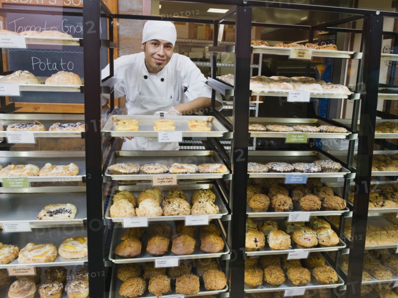Baker standing behind trays of baked goods. Photo. Erik Isakson