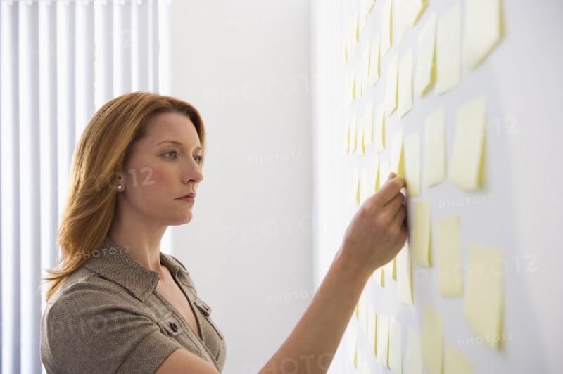Businesswoman putting sticky note on wall.