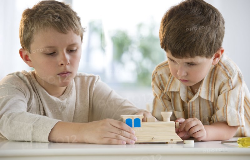 Two young boys building a wooden train.