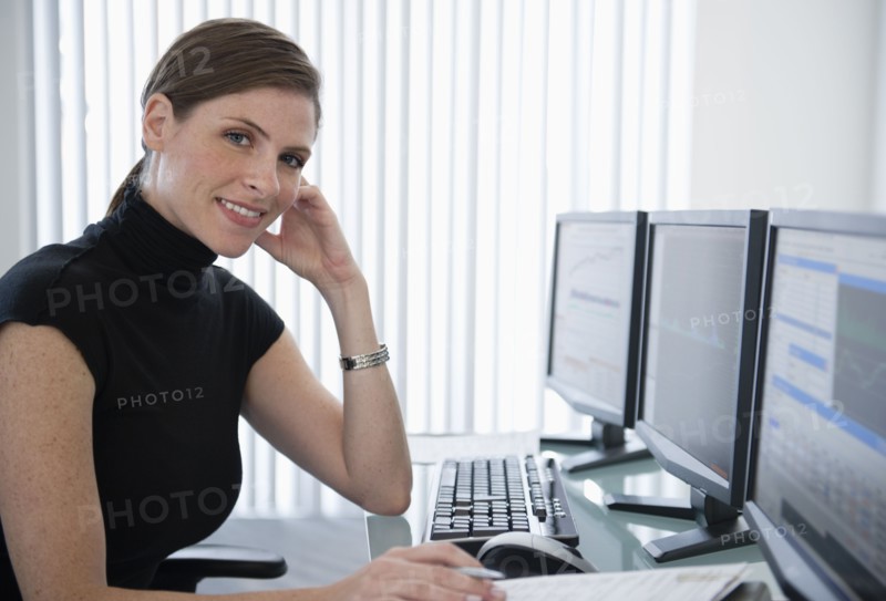 Woman in office sitting at desk with computers.