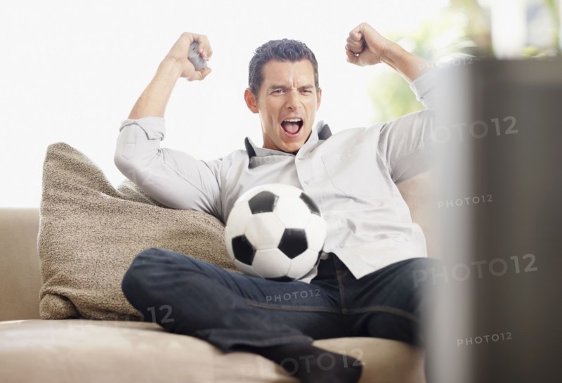 Mid adult man watching football match on television. Photo : Momentimages