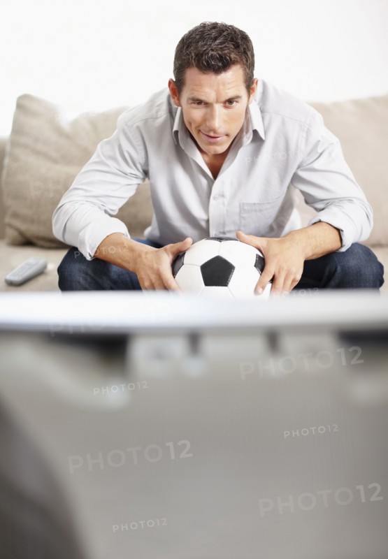 Mid adult man watching football match on television. Photo : Momentimages