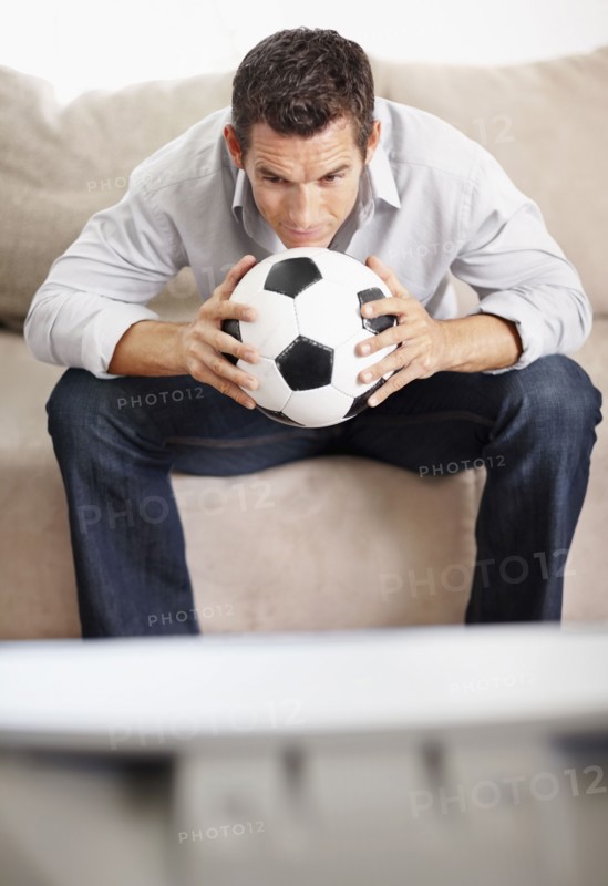 Mid adult man watching football match on television. Photo : Momentimages