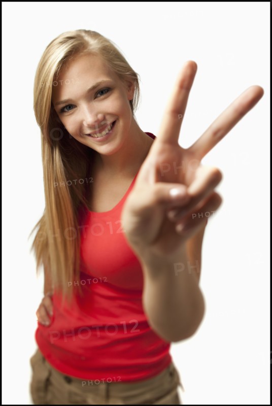 Young woman on white background showing peace sign. Photo : Mike Kemp