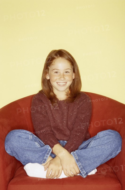 Cute young girl sitting in red chair. Photo : Fisher Litwin