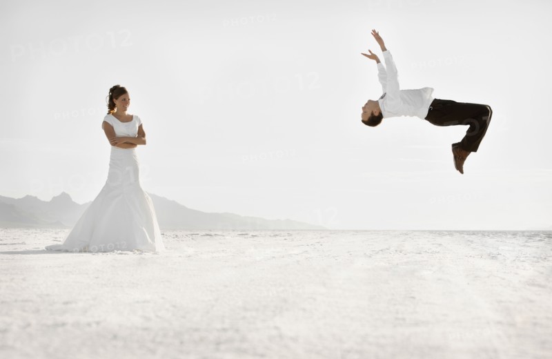 Bride watching groom performing backflip in desert. Photo : FBP