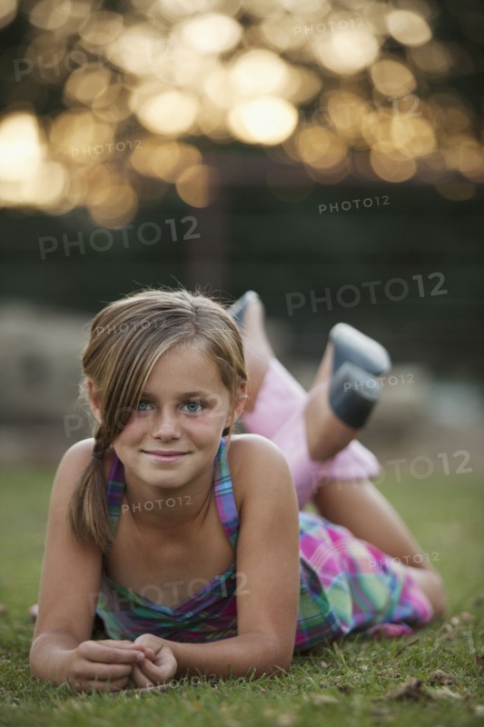 Portrait of girl (8-9) lying on grass. Photo : Mike Kemp