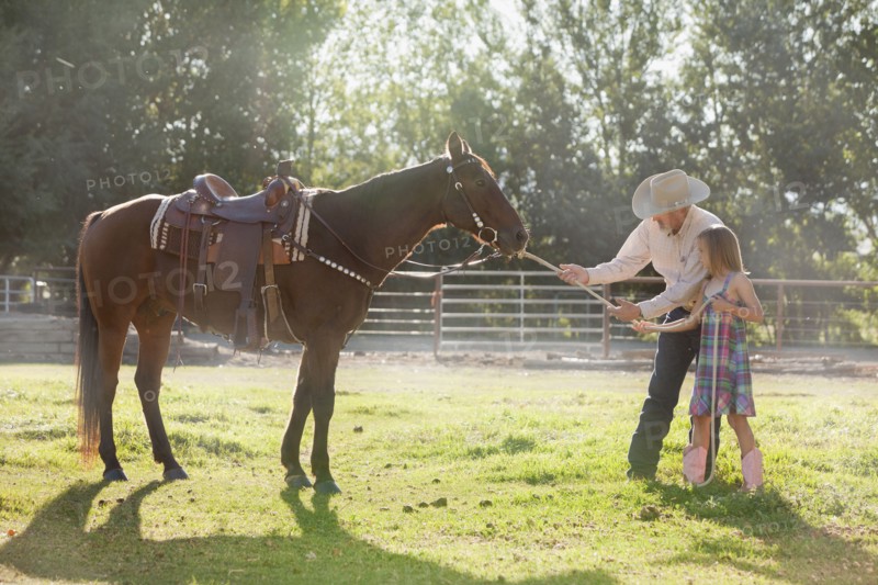Senior man with granddaughter (8-9) training horse in ranch. Photo : Mike Kemp