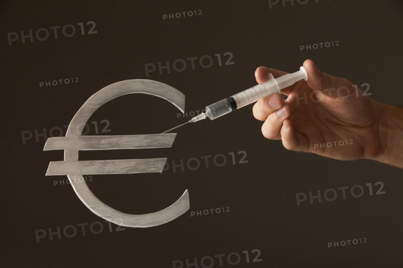 Hand holding syringe on "Euro" sign. Photo : Mike Kemp