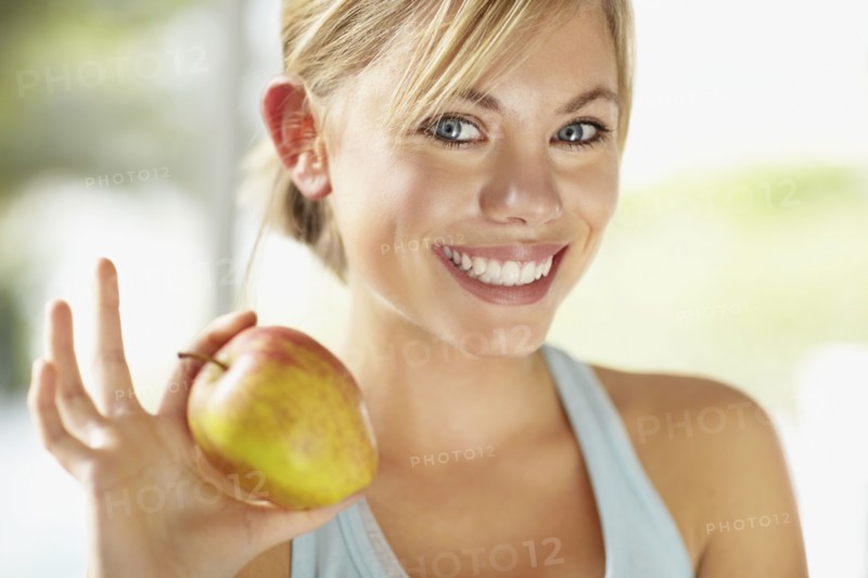 Portrait of young blonde woman holding apple. Photo : Momentimages