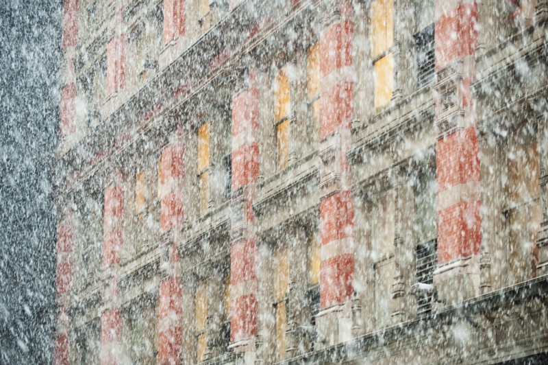 Snow falling in front of apartment building.