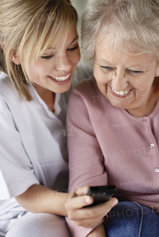 Daughter and mother checking mobile phone and smiling. Photo : Momentimages
