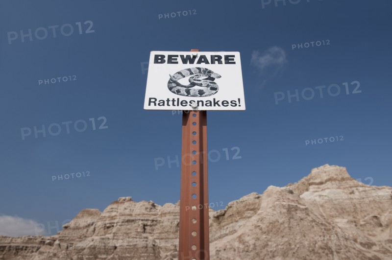 USA, South Dakota, Badlands National Park, Rattlesnake warning sign against sky, mountain in background.
