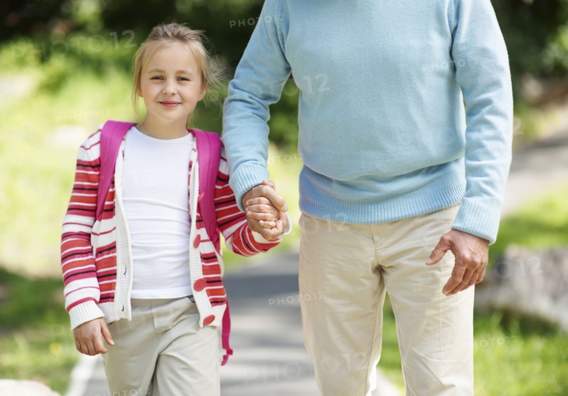 Granddaughter (10-11) and grandfather walking through parkholding hands. Photo : Momentimages