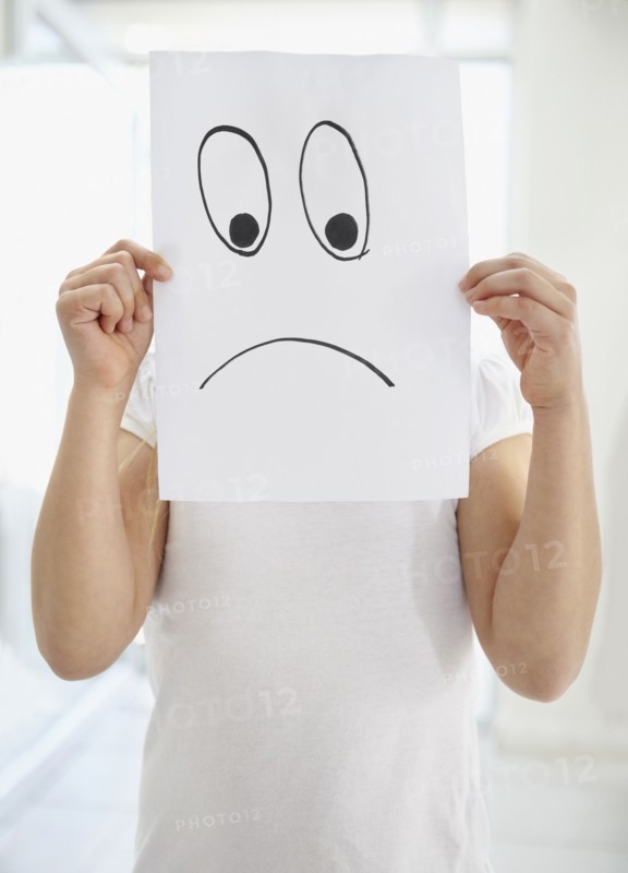 Girl (10-11) girl holding 'sad face' in front of herself. Photo : Momentimages