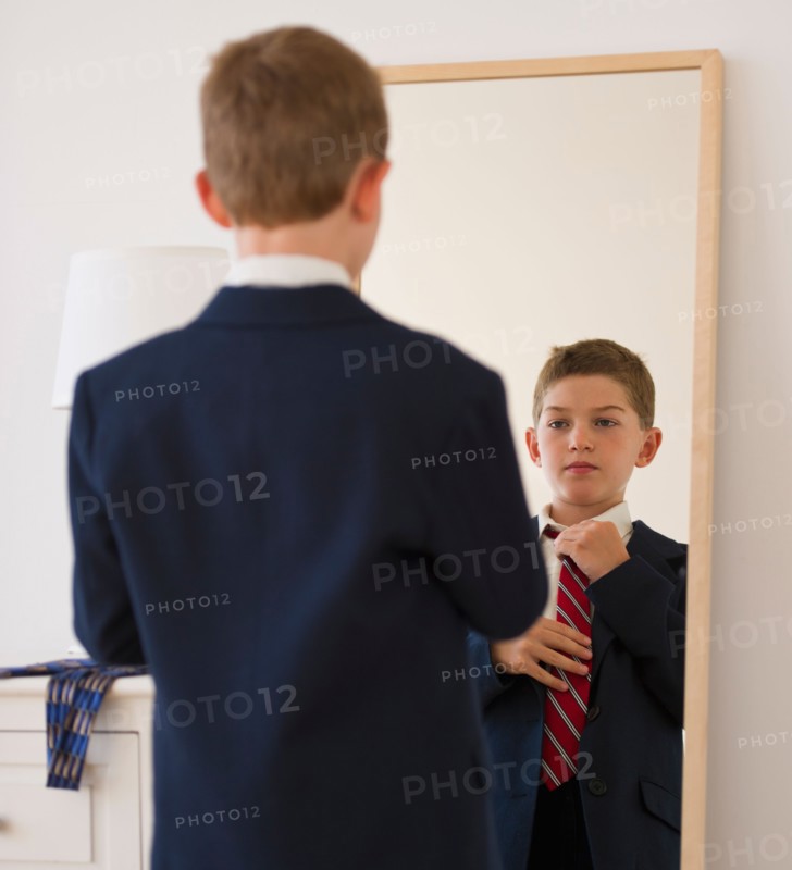 Boy (10-11) adjusting tie in front of mirror. Photo : Daniel Grill