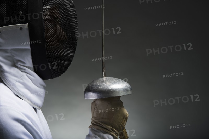 Studio portrait of fencer holding fencing foil.