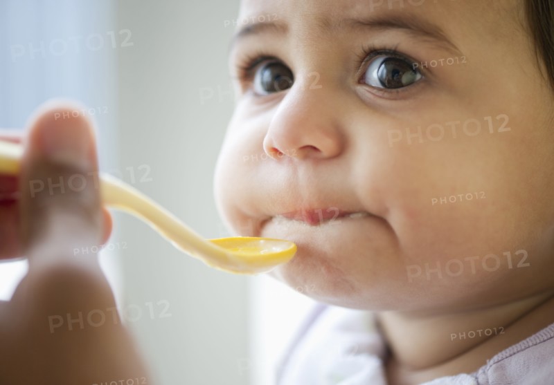 Baby girl (12-18 months) eating from plastic spoon.