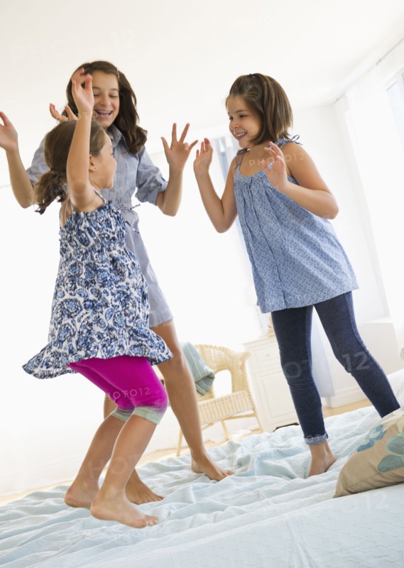 Sisters (2-3, 8-9, 12-13) jumping on bed. Photo : Daniel Grill
