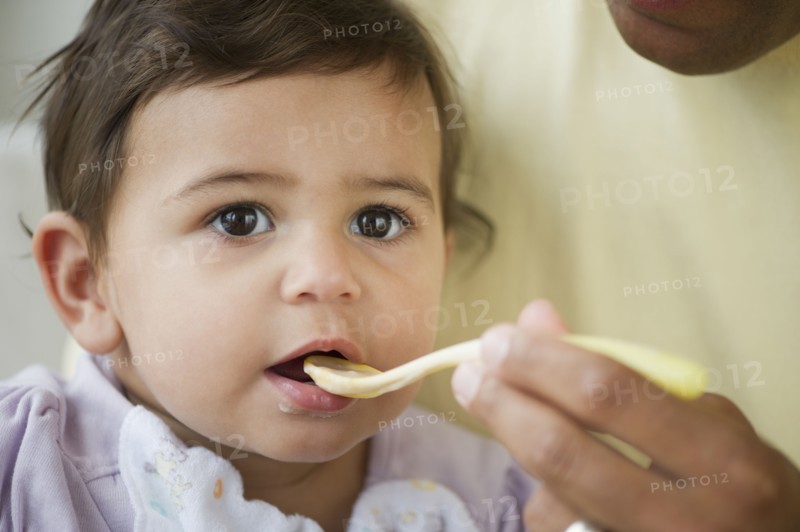 Baby girl (12-18 months) eating from plastic spoon.