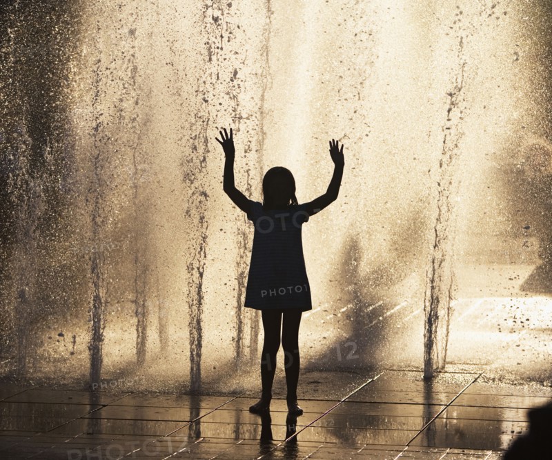 Silhouette of girl playing in fountain. Photo : fotog