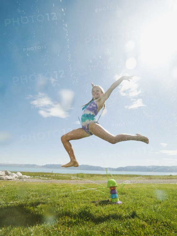 Girl (8-9) jumping over watering system.
