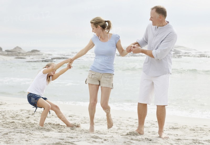 Girl (10-11) playing on beach with parents. Photo : Momentimages