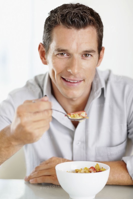 Cheerful mid adult man eating cornflakes. Photo : Momentimages