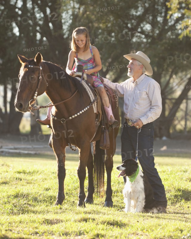 Senior man with dog assisting granddaughter (8-9) horseback riding in ranch. Photo : Mike Kemp