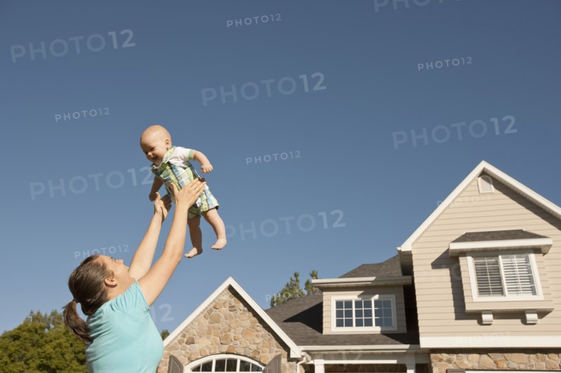 Mother lifting baby boy (6-11 months) outside home. Photo : FBP