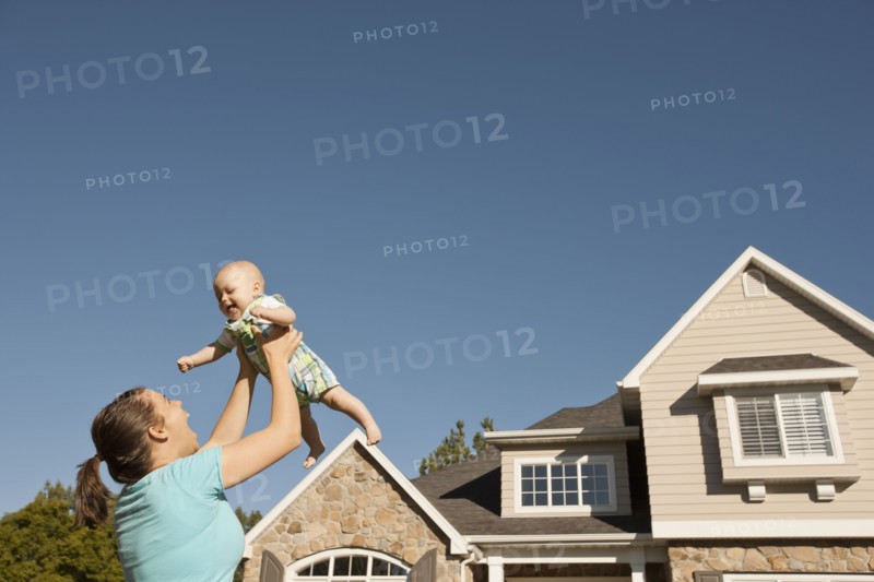 Mother lifting baby boy (6-11 months) outside home. Photo : FBP