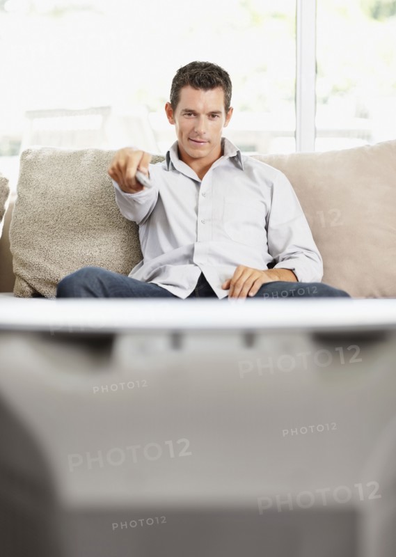 Mid adult man in front of televisionchanging channels. Photo : Momentimages
