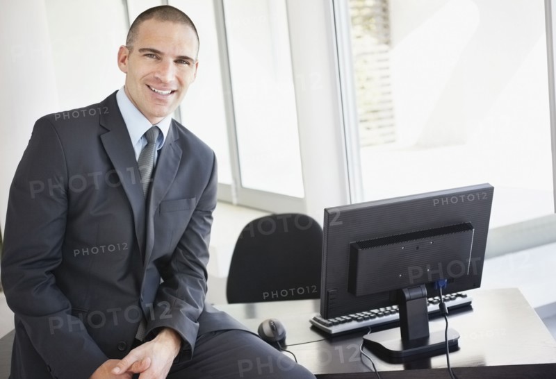 Businessman sitting on office desk. Photo : Momentimages
