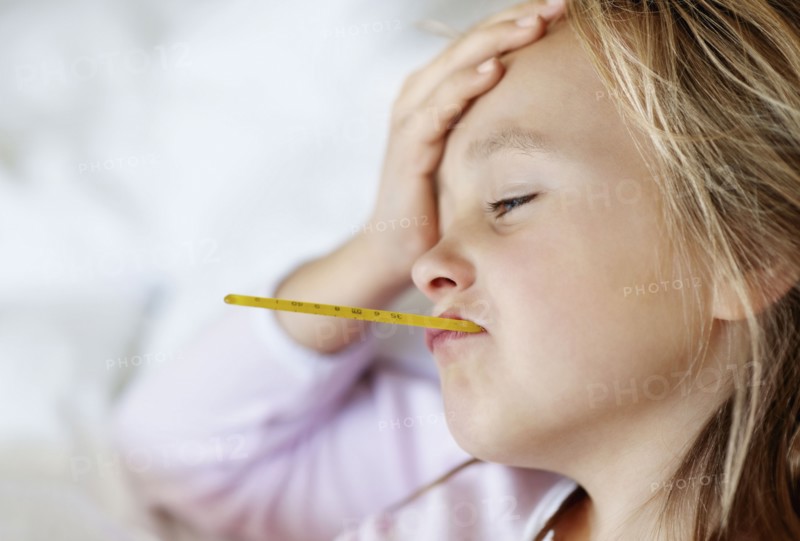 Sad girl (10-11) lying in bed with thermometer in mouth. Photo : Momentimages
