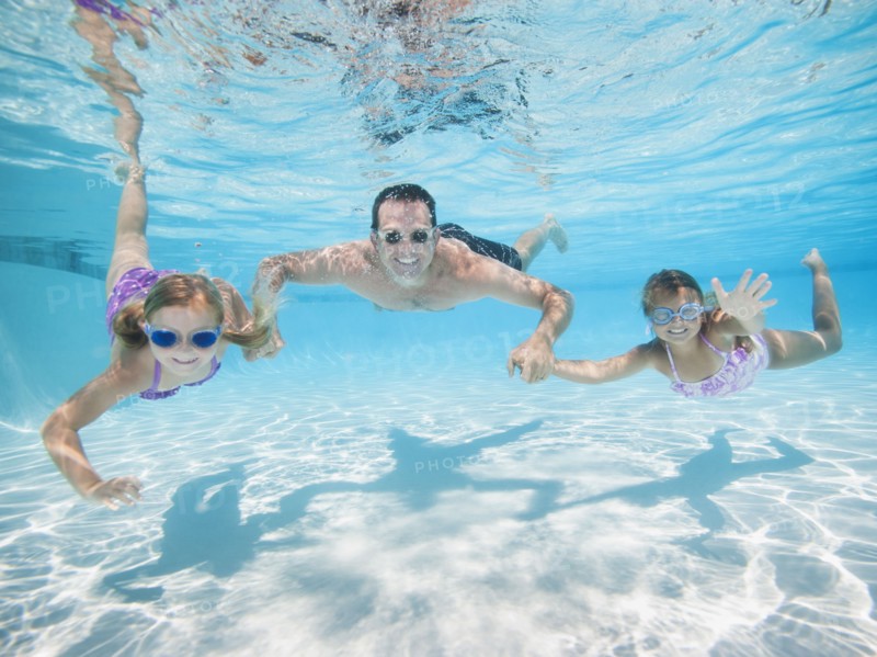 Father with two daughters (6-7,8-9) swimming underwater.