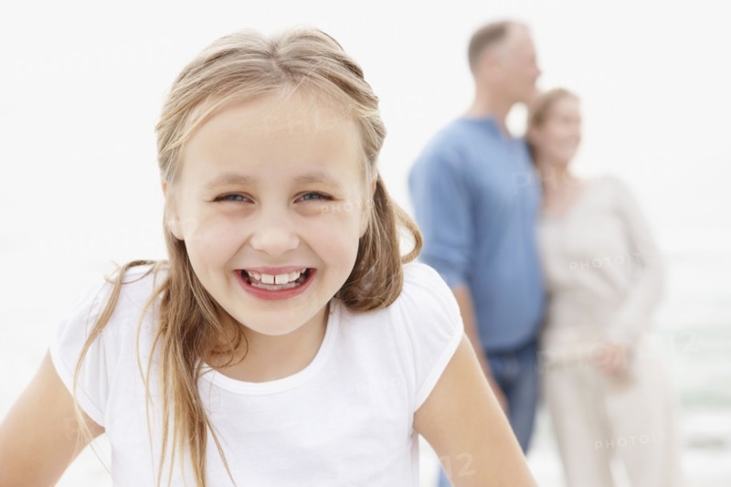 Portrait of smiling girl (10-11), embracing couple in the background. Photo : Momentimages