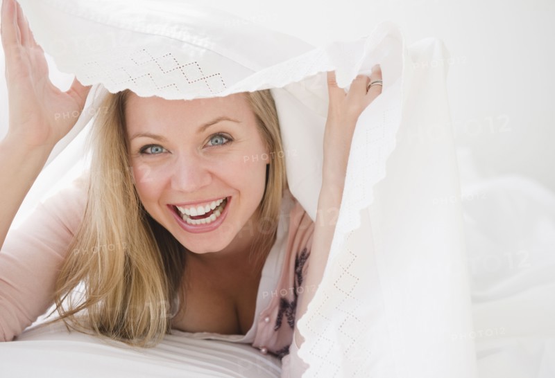 USA, New Jersey, Jersey City, Laughing attractive young woman emerging from under quilt. Photo : Jamie Grill Photography