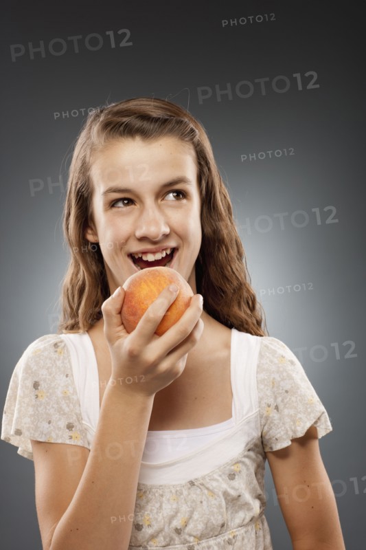 Girl (12-13) holding peach and laughing, studio shot. Photo : FBP